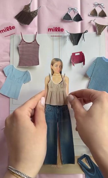 Boneca de papel sendo vestida com regata e calça jeans, com outras roupinhas em volta